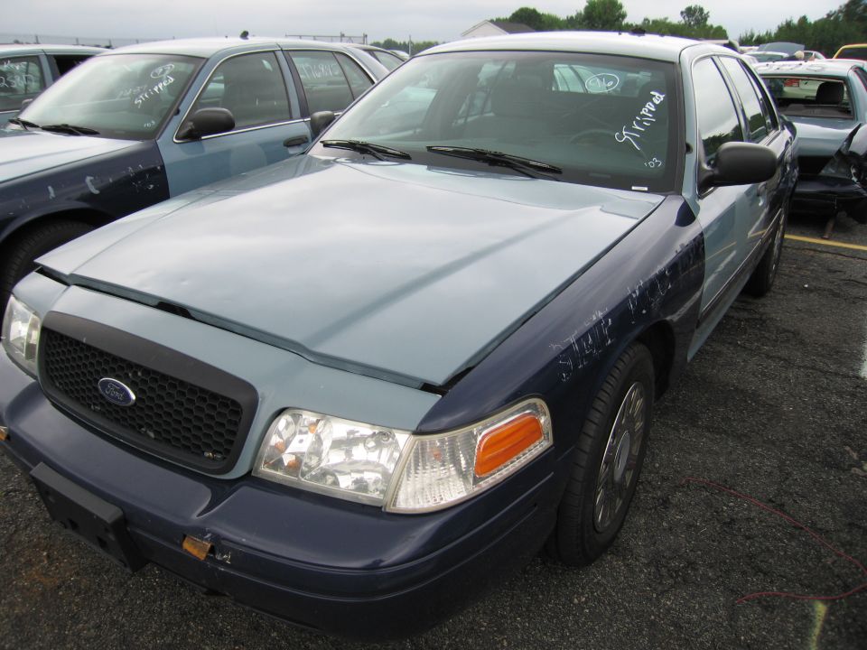 Front view of a two-tone Ford Crown Victoria, one of several cars in a lot. White writing on windshield says 'STRIPPED' and '03'