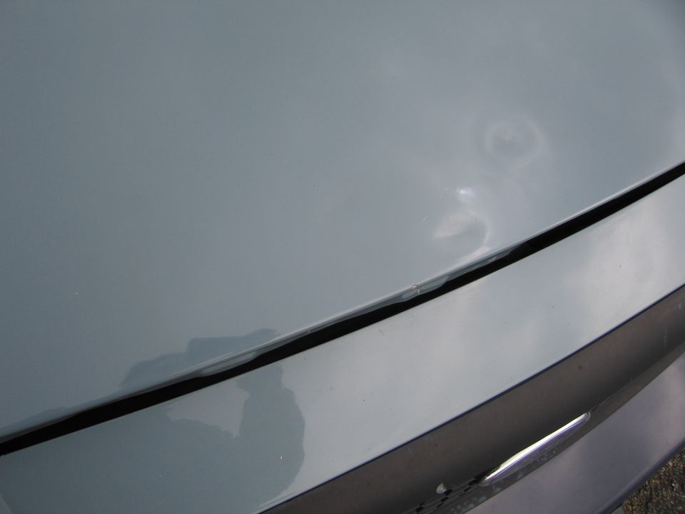 Close-up of a light blue car hood with a dent and paint chip near the seam