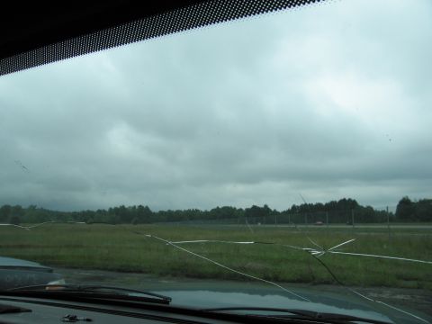 2001 Ford Crown Victoria - View through a cracked windshield shows a cloudy sky over a field and distant trees.