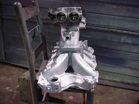 1979 Ford Bronco - Engine intake manifold with dual throttle bodies, likely for a V8 engine, sits on a chair.
