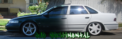 1993 Ford Taurus - A two-tone Ford Taurus sedan with aftermarket wheels is parked on a residential street.