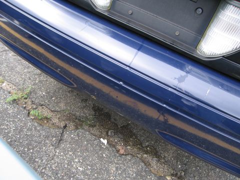 2001 Ford Crown Victoria - Close-up photo of a dark blue vehicle's rear bumper and taillight over broken asphalt.