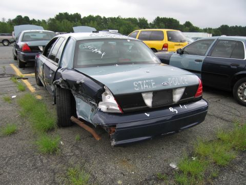 2001 Ford Crown Victoria - Photo of a damaged blue State Police sedan with crash damage parked in an auction lot.