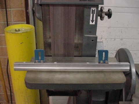 1979 Ford Bronco - A metal jig is positioned on a belt sander, next to a yellow cylindrical object. The registry claims this is a 1979 Ford Bronco, but the im…