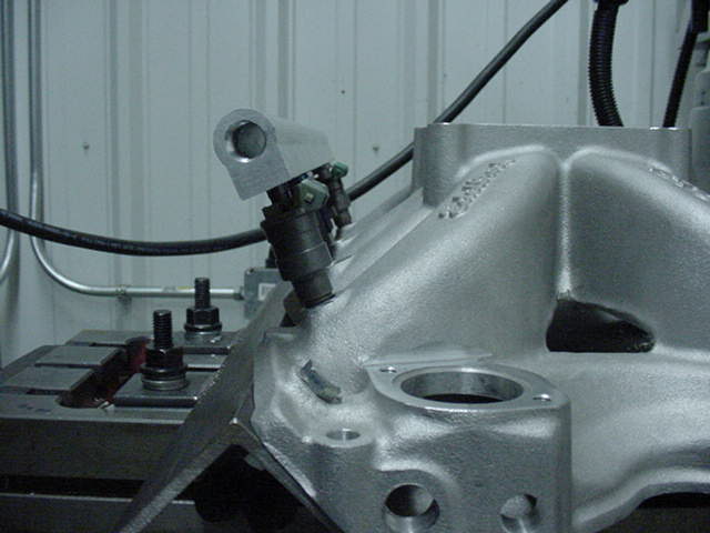 Close-up of a fuel injector mounted on an aluminum intake manifold, likely during an engine build or modification