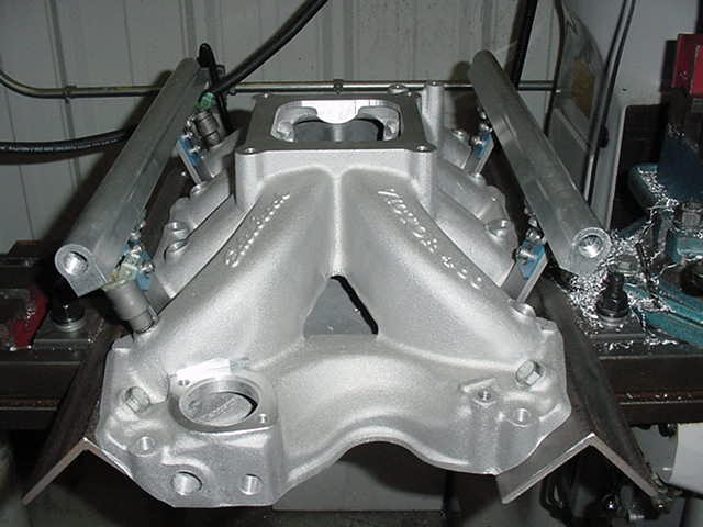 Close-up of an aluminum intake manifold with fuel injectors attached, sitting on a workbench