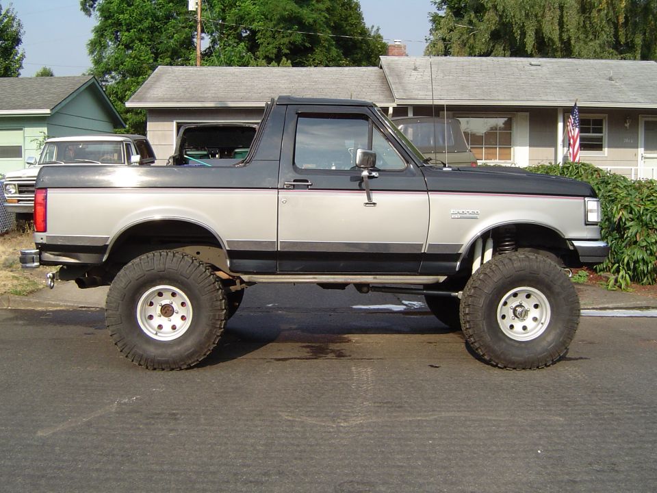 Lifted two-tone black and silver Ford Bronco parked on a residential street, side view