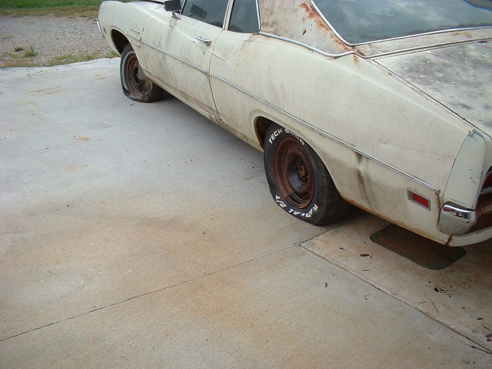 Rusty cream two-door classic car on a driveway with bare steel wheels and raised-white-letter tires