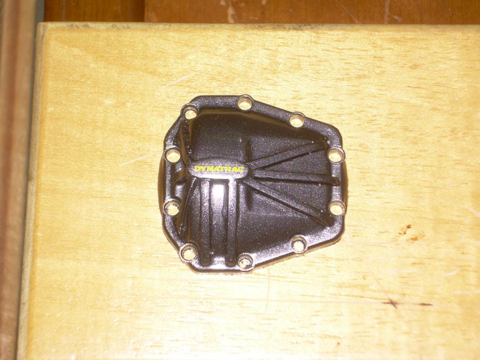Black differential cover with yellow DYNA TRAC text on a wooden surface.