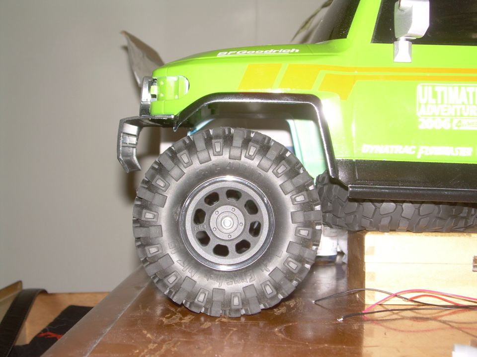 Green RC off-road vehicle, front wheel and fender detail, yellow stripes, "ULTIMATE ADVENTURE" text
