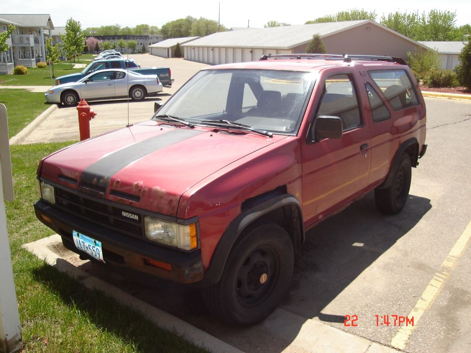Red 1990s Nissan Pathfinder with black stripe on hood, parked in a lot.
