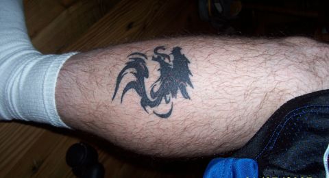 1994 Ford Bronco - A close-up shot of a black tribal tattoo of a bird or phoenix on a hairy leg, which is partially covered by a white sock and blue athletic…
