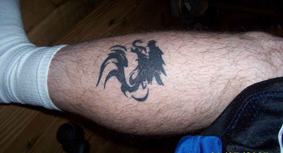 Black tribal bird tattoo on a hairy leg with white sock and blue shorts.