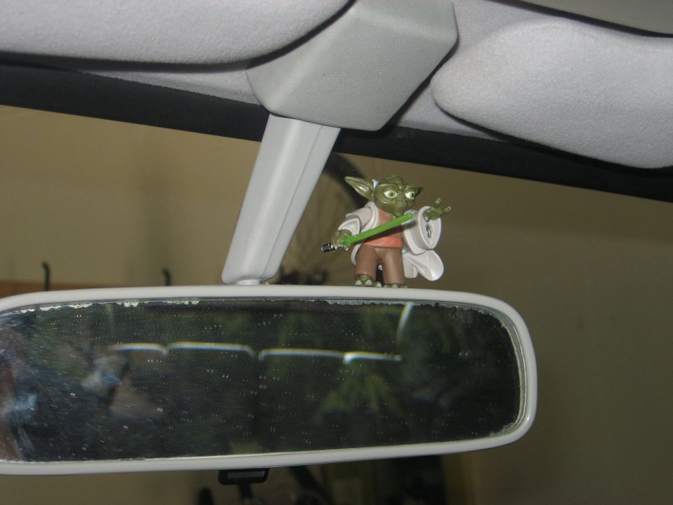 Yoda figurine with a green lightsaber on a car's rearview mirror.
