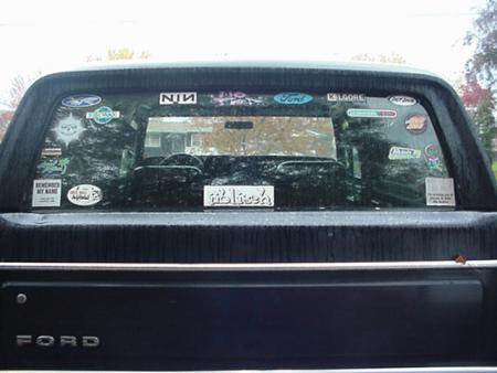 1979 Ford Bronco - Rear window of a black Ford truck adorned with numerous stickers, obscuring the interior.