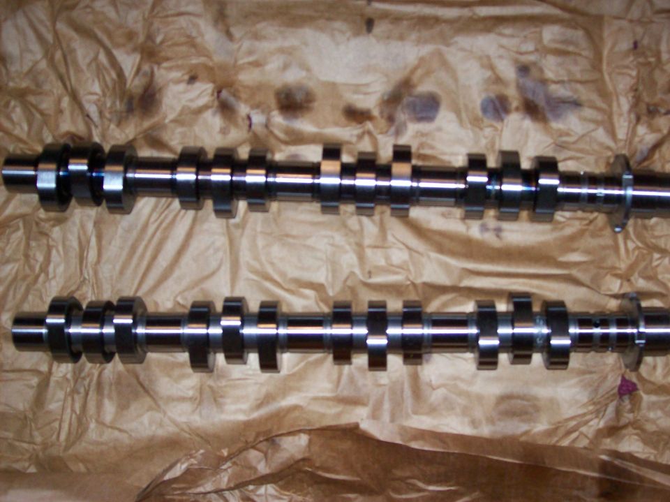 Two metal camshafts with multiple lobes on brown paper