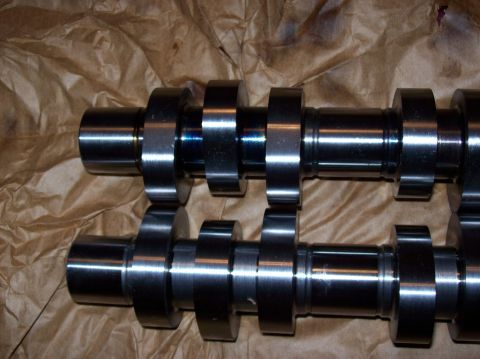 2007 Ford Mustang - Two camshafts are laid out on brown paper. The camshafts are made of metal and have multiple lobes and journals.