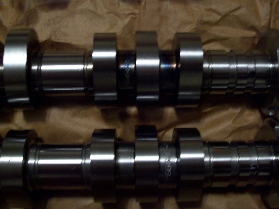 Two metal camshafts with multiple lobes on brown paper