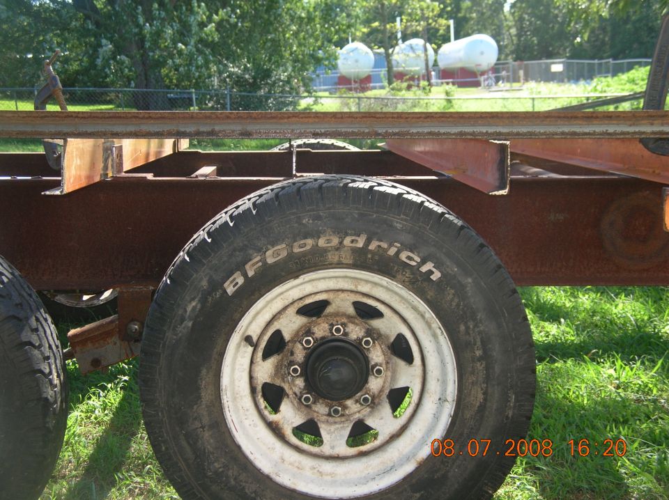 BFGoodrich tire on a rusty trailer frame with propane tanks in the background.