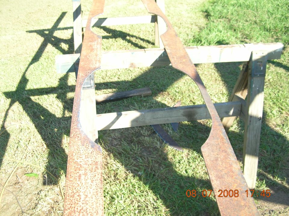 Two rusty, cut metal pieces on a sawhorse outdoors.