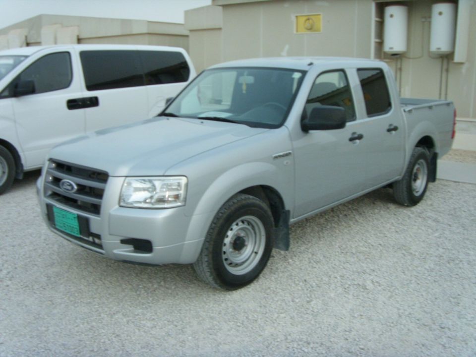 Silver Ford double-cab pickup on gravel with steel wheels and green license plate