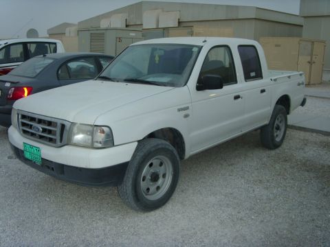 1978 Ford Bronco - A white Ford Ranger double-cab pickup photographed from the front three-quarter angle on a gravel lot, wearing a green Middle Eastern-style…