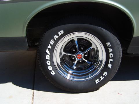 1973 Ford Ranchero - Close-up of a chrome-and-black Magnum 500-style five-spoke wheel with a red center cap, wrapped in a raised-white-letter Goodyear Eagle GT…