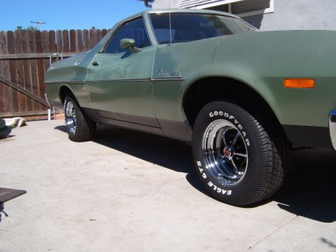 1973 Ford Ranchero - A close-up, low-angle side view of a vintage green Ford Ranchero parked on a concrete driveway. The vehicle features chrome wheels and Good…