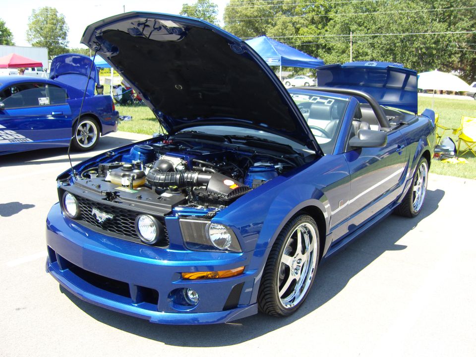Photo of a blue Ford Mustang GT convertible with hood open at a car show