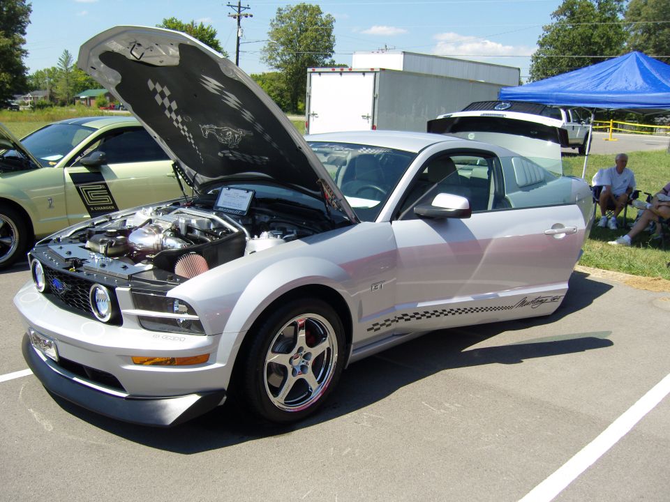 Silver supercharged S197 Ford Mustang GT with hood and door open at a car show
