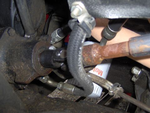 1978 Ford Bronco - A close-up view shows a U-joint connecting to a steering component, with a braided hose and a rusty metal rod visible. A white oil filter w…