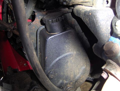 1978 Ford Bronco - A close-up view of a black power steering fluid reservoir and cap, mounted within a dusty engine bay. A thick black hose runs diagonally ac…