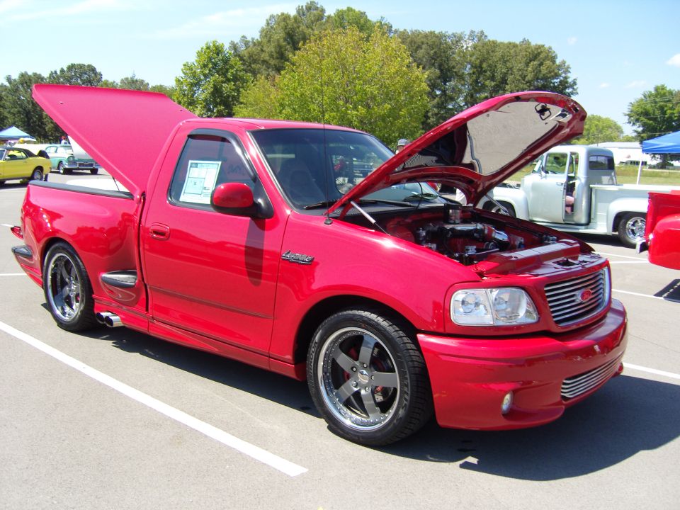 Red Ford F-150 SVT Lightning pickup with hood open in a show parking lot