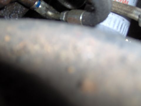 1978 Ford Bronco - A close-up, blurry shot shows a white oil filter with a ribbed edge, partially obscured by a metal hose and a dark, out-of-focus foreground…