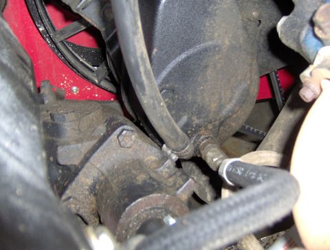 1978 Ford Bronco - A close-up view of the engine bay of a vehicle, showing various hoses, a black pulley housing, and a red component behind a belt.
