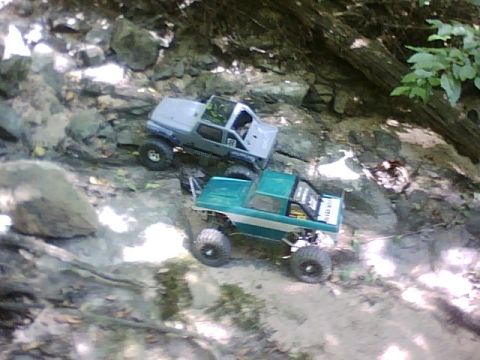 1996 Ford Bronco - Two RC trucks tackle an off-road course, one green with white stripes and the other gray.