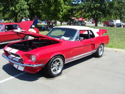 2007 Ford Mustang - A red classic convertible with racing stripes and a white top is parked at an outdoor event.