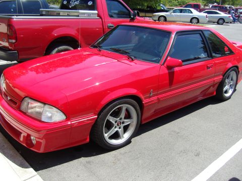 2007 Ford Mustang - A red coupe with a distinctive body style is parked next to a red pickup truck.