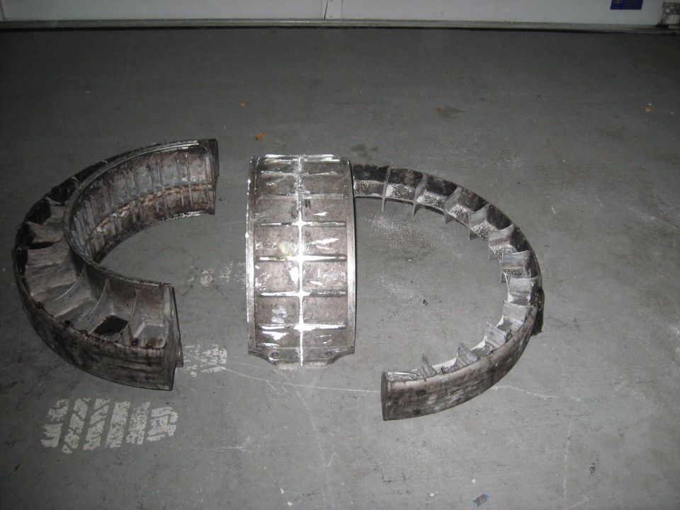 Three pieces of a damaged turbine fan, likely from an aircraft engine, lying on a concrete floor