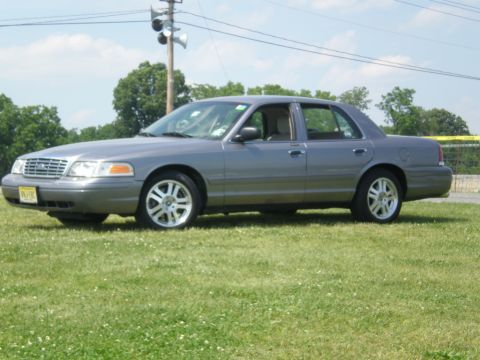 1988 Mercury Grand Marquis - A gray sedan is parked on a grassy field under a partly cloudy sky.