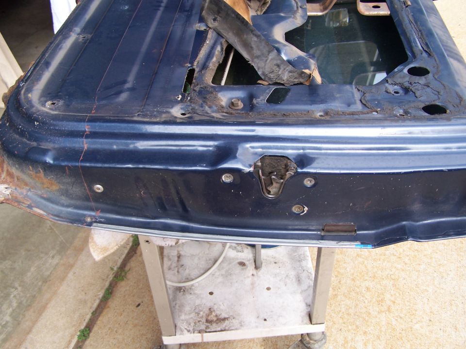Blue car door with rust and damage, showing latch mechanism