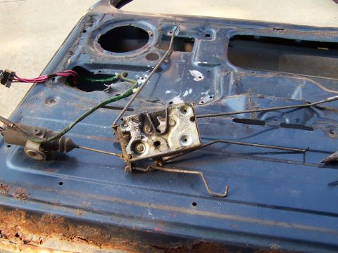 1986 Ford Bronco - Interior view of a heavily rusted car door showing the latch mechanism and electrical wiring.