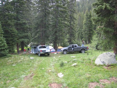 2004 Ford F-150 - Two pickup trucks are parked at a campsite in a forest, with tents set up nearby.