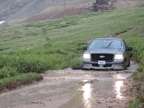 2004 Ford F-150 - 2004 Ford F-150 navigates a water obstacle in a mountainous, grassy area.