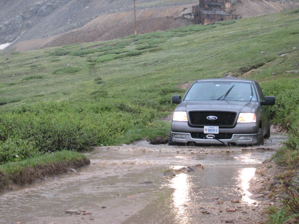 2004 Ford F-150 driving through a muddy water crossing on a mountain road