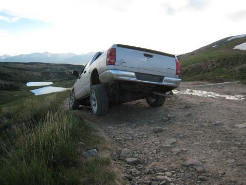 2004 Ford F-150 - A silver Dodge pickup truck navigates a rough, rocky terrain with lakes and mountains in the background.