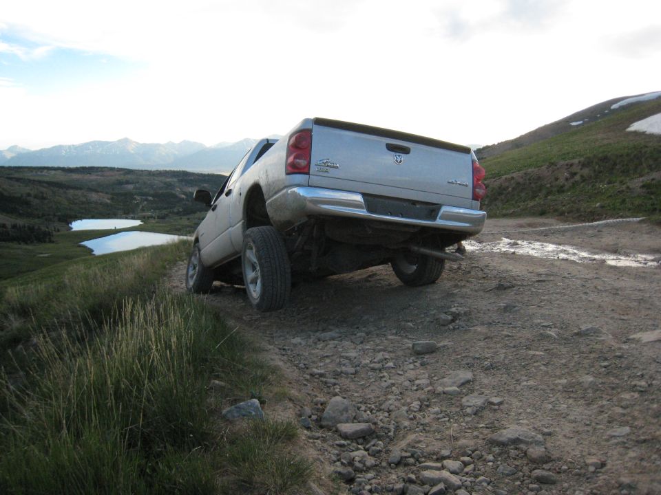 Silver pickup truck on a rocky mountain road, rear view. Dodge logo visible on tailgate