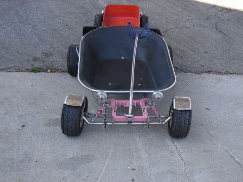 1973 Ford Ranchero - A hot-rod-style pedal car or kids' cart shot head-on from above, built with a black tub body, chrome tube frame and pink-painted front axle…