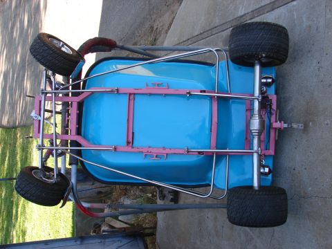 1973 Ford Ranchero - Overhead view of a small pink-framed go-kart with a light blue plastic body tub, photographed sideways on a concrete driveway next to grass…
