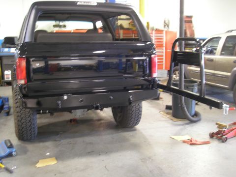 1995 Ford Bronco - Rear view of a black Ford Bronco with a custom bumper and tire carrier in a garage.